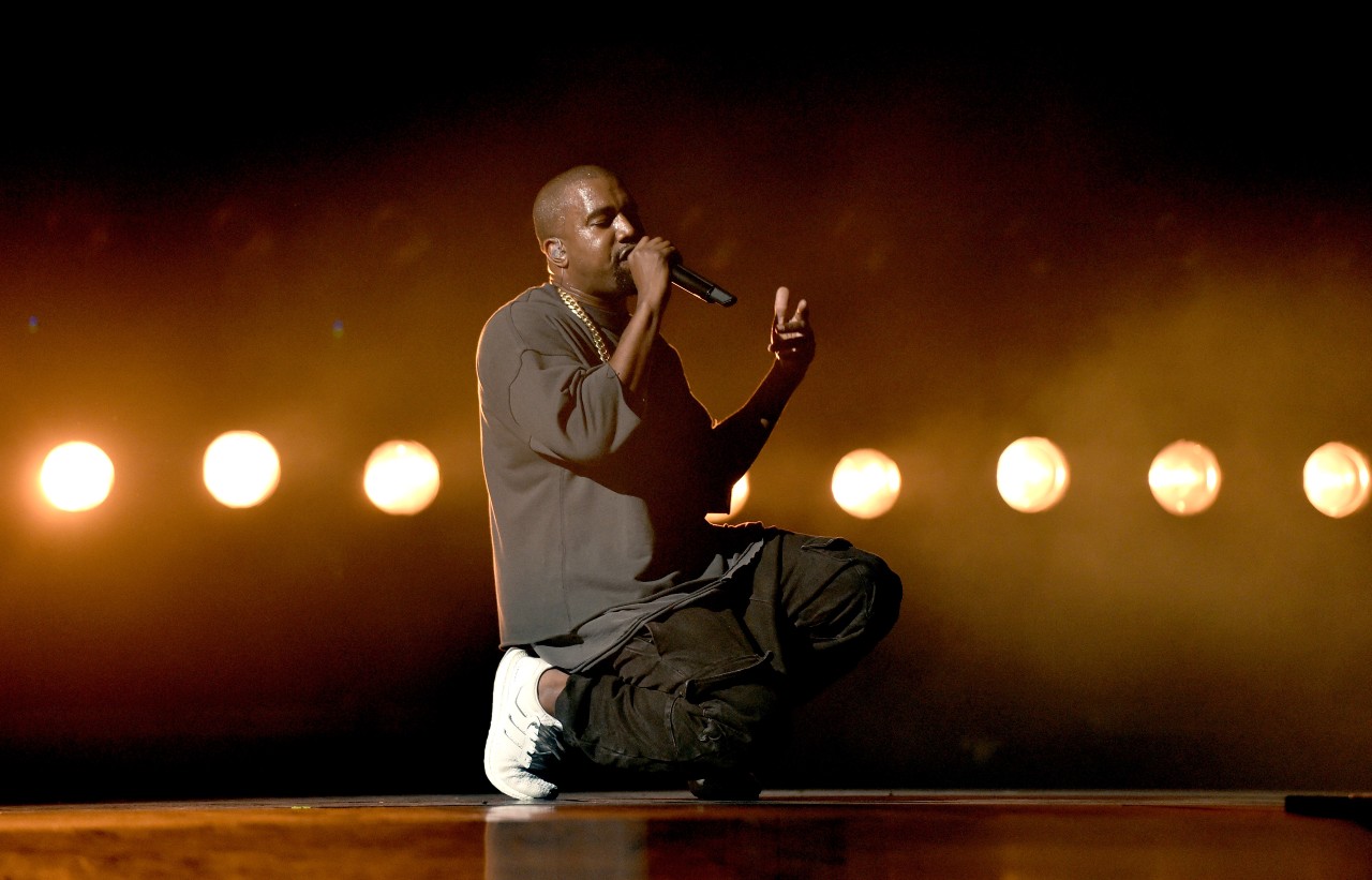 Kanye West kneels while performing a song.