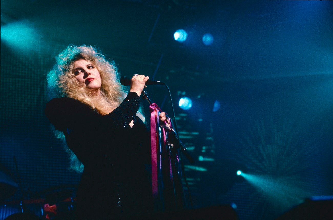 Stevie Nicks holds a microphone with a ribbon tired around it.