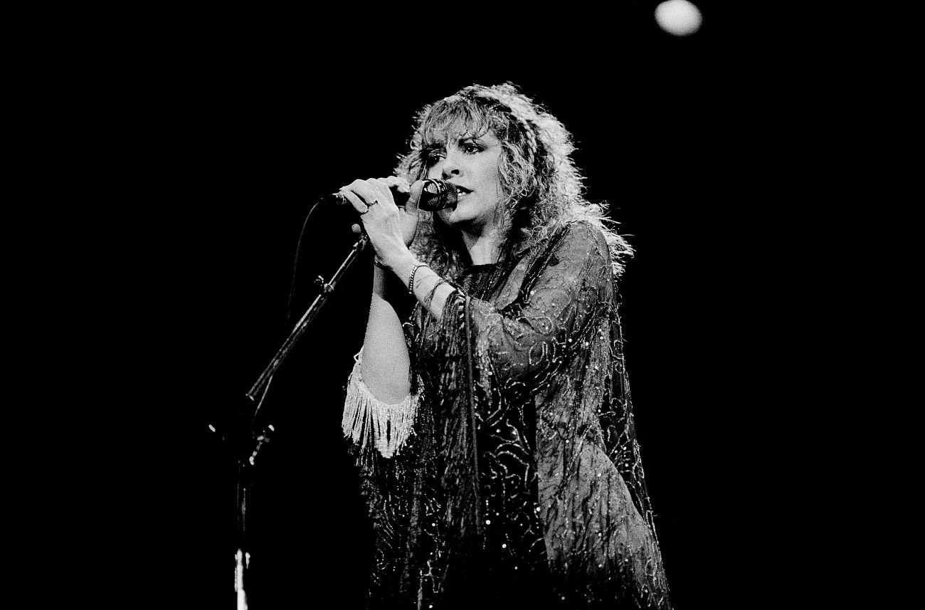 A black and white picture of Stevie Nicks holding a microphone and singing. 