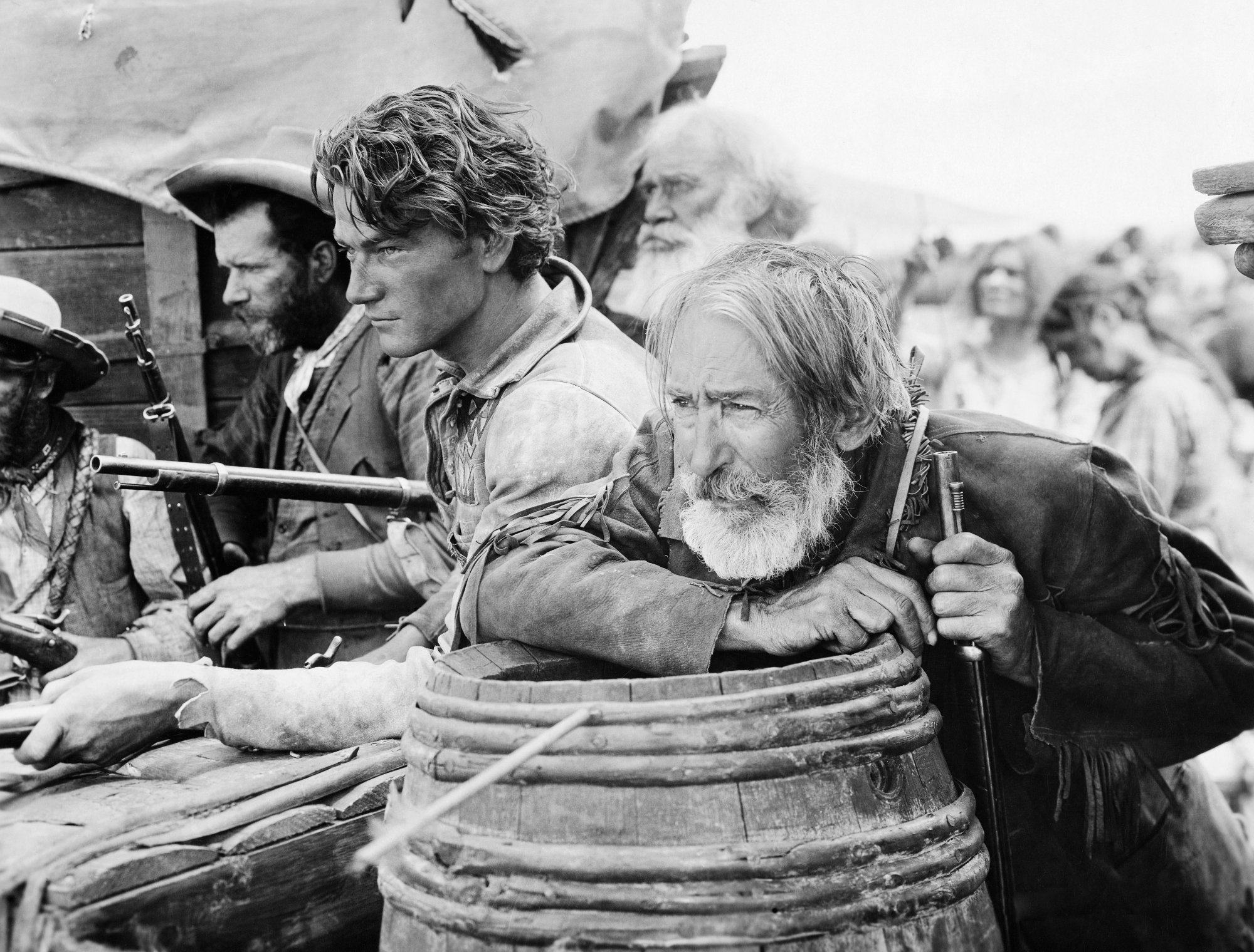 'The Big Trail' John Wayne Breck Coleman and Tully Marshall as Zeke on movie set. Black-and-white photo of Wayne and Marshall crouching behind barrels with guns.