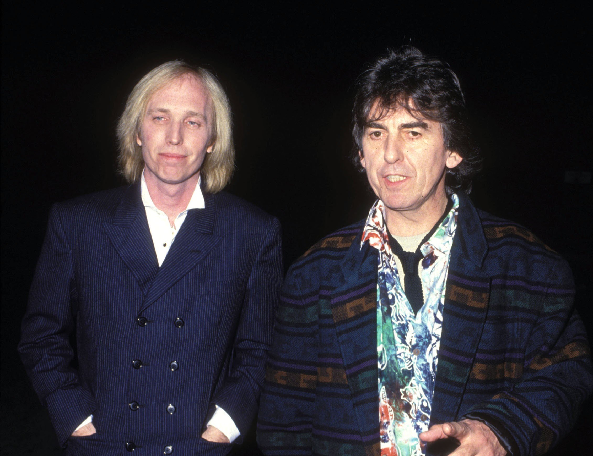 Tom Petty and George Harrison wear black jackets and walk together.