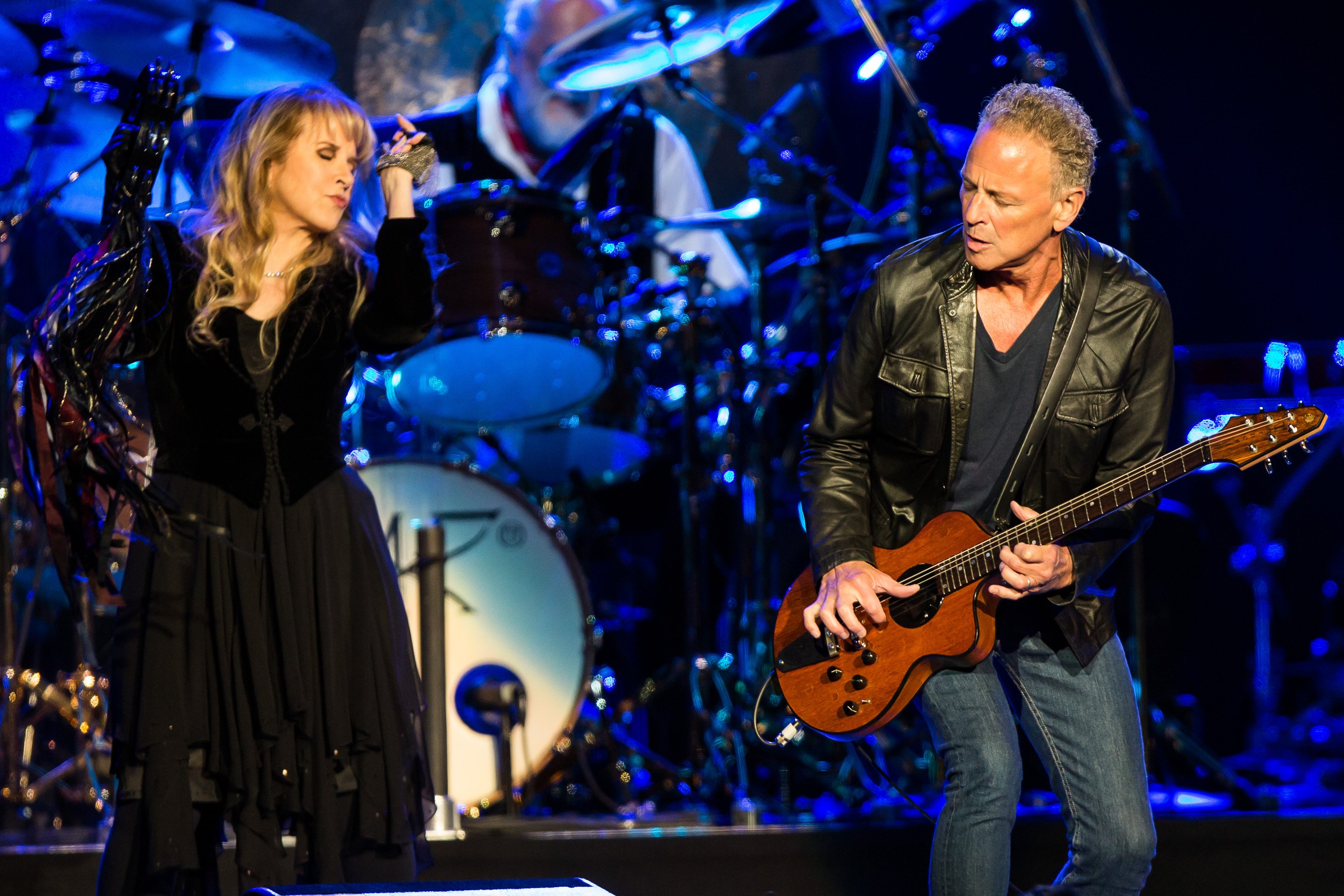 Stevie Nicks plays the tambourine while standing next to Lindsey Buckingham as he plays guitar.