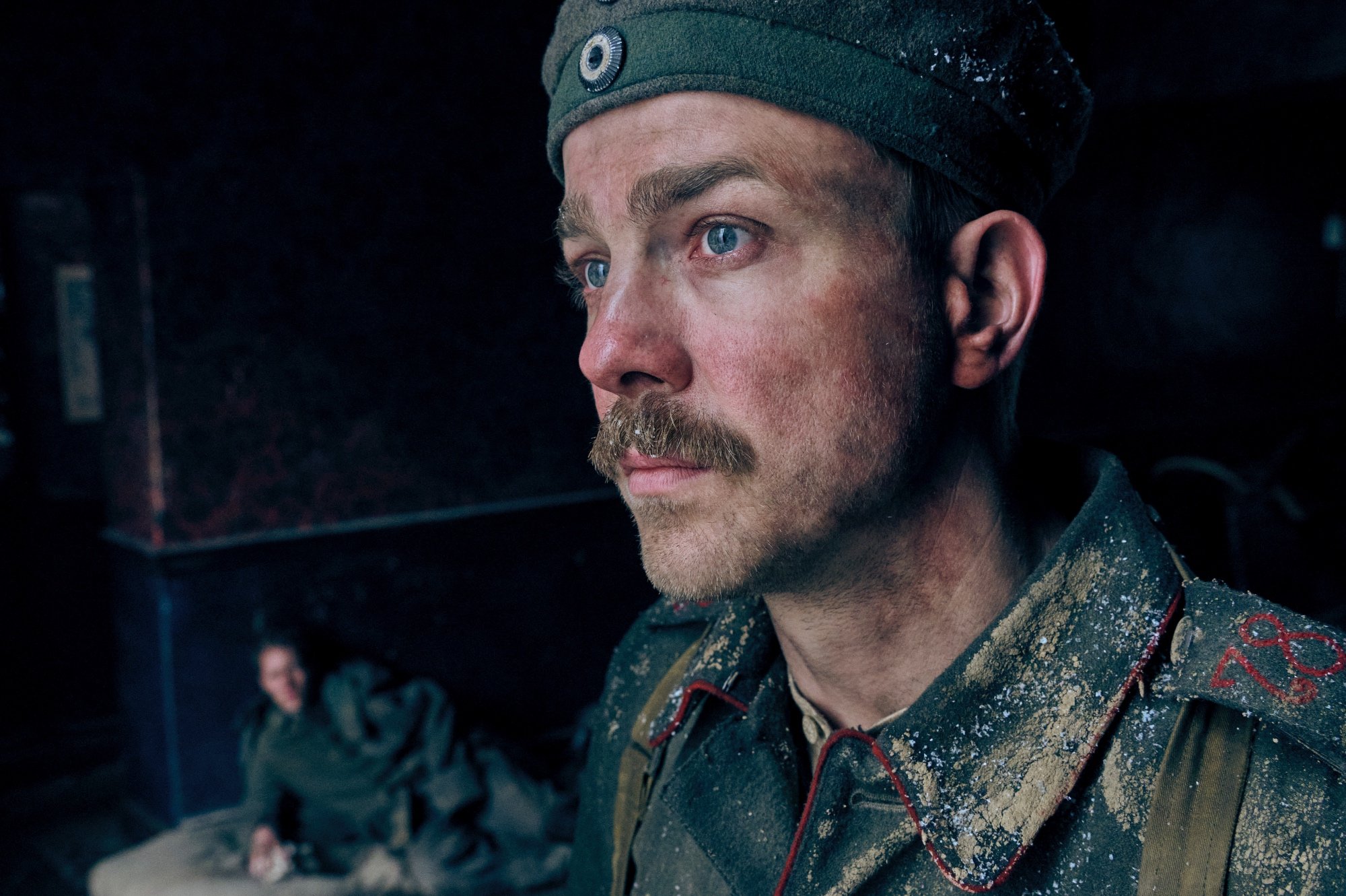 'All Quiet on the Western Front' Felix Kammerer as Paul Bäumer and Albrecht Schuch as Kat wearing their military uniforms. Schuch is standing closer to the camera, looking off-camera. Kammerer is laying down on the ground in the background.