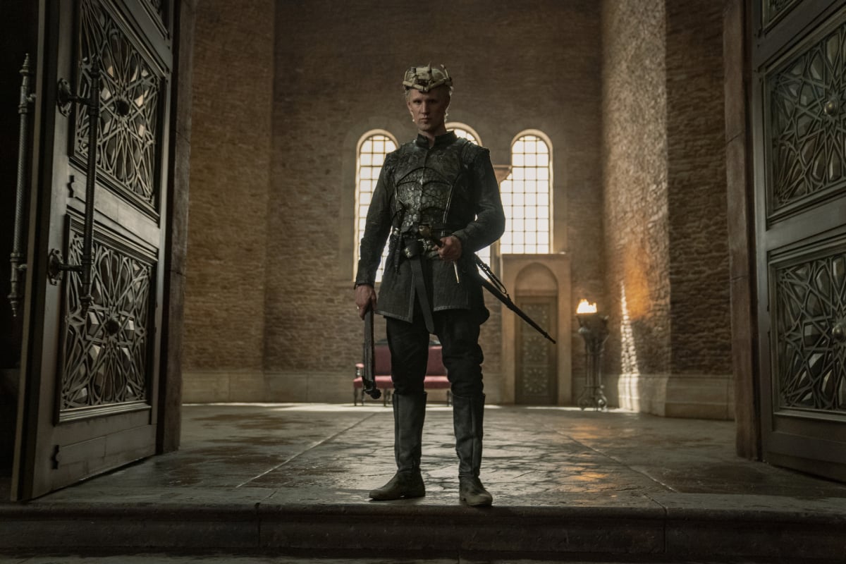 Matt Smith as Daemon Targaryen in House of the Dragon. Daemon stands at the doorway to the throne room wearing armor and a crown.