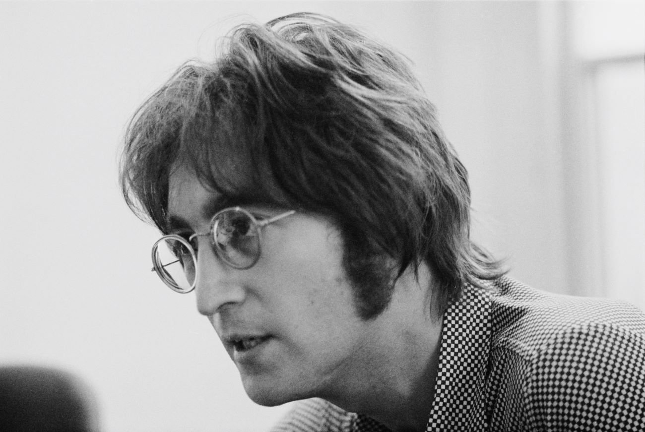 A black and white picture of John Lennon wearing a checkered shirt and wearing glasses.