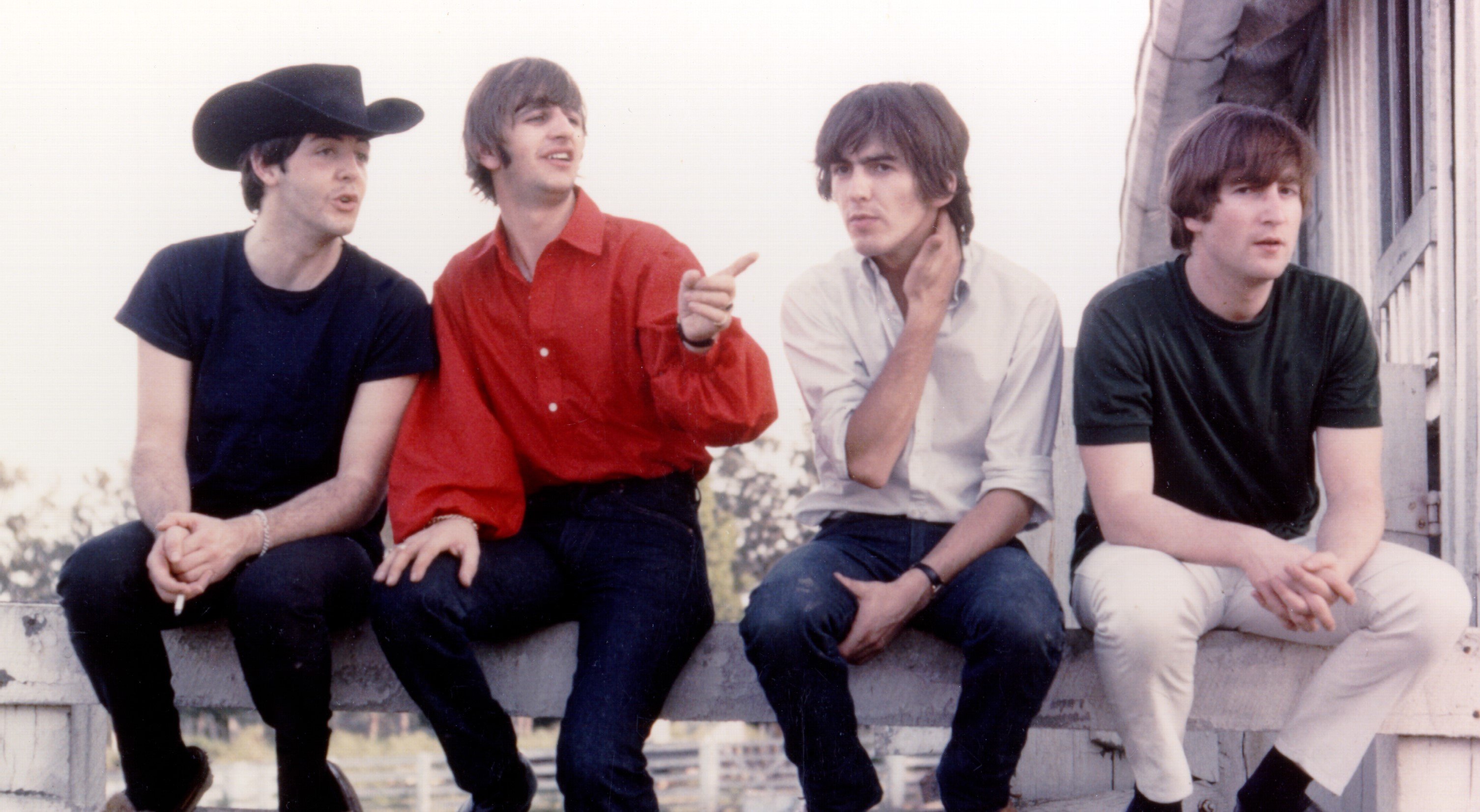 The Beatles' Paul McCartney, Ringo Starr, George Harrison, and John Lennon on a fence