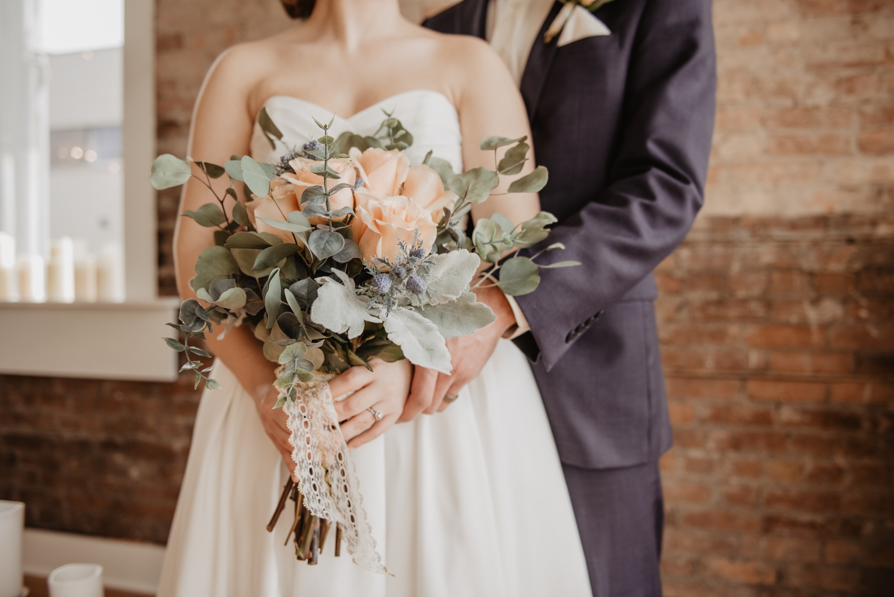 A bride in a wedding dress and a groom in a gray suit stand together at their wedding ceremony.