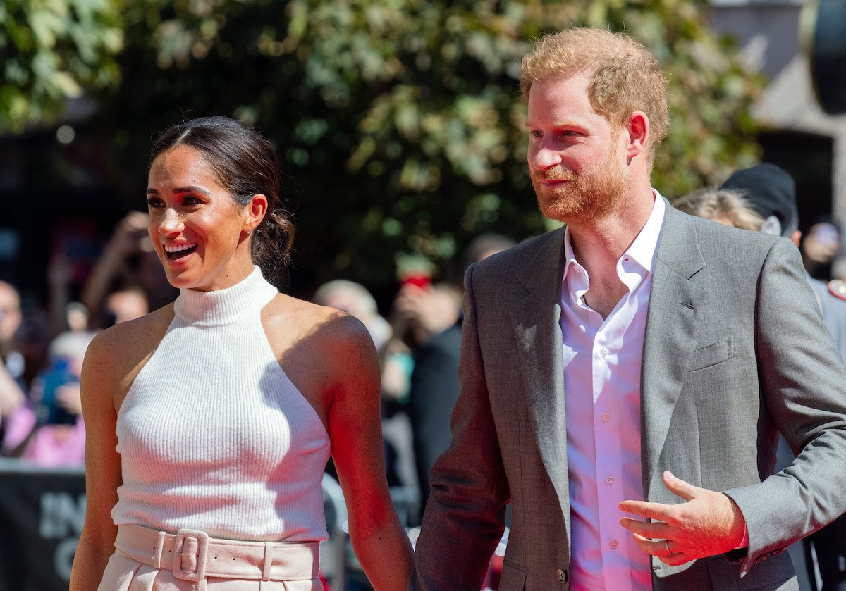 Meghan Markle and Prince Harry, whose 2020 exit prompted a guidebook to tell private secretaries to ask themselves one question according to Valentine Low's 'Courtiers' book, walk next to each other and look on in Germany