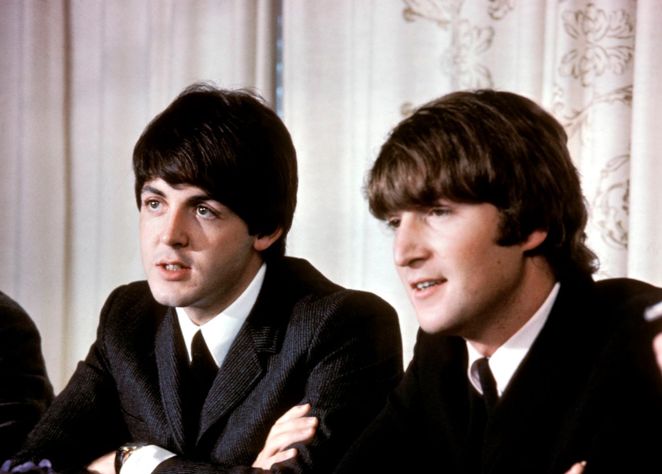 Paul McCartney and John Lennon sit at a table together. 