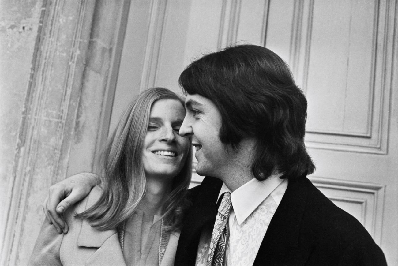 A black and white picture of Paul McCartney standing with his arm around Linda McCartney's shoulders.