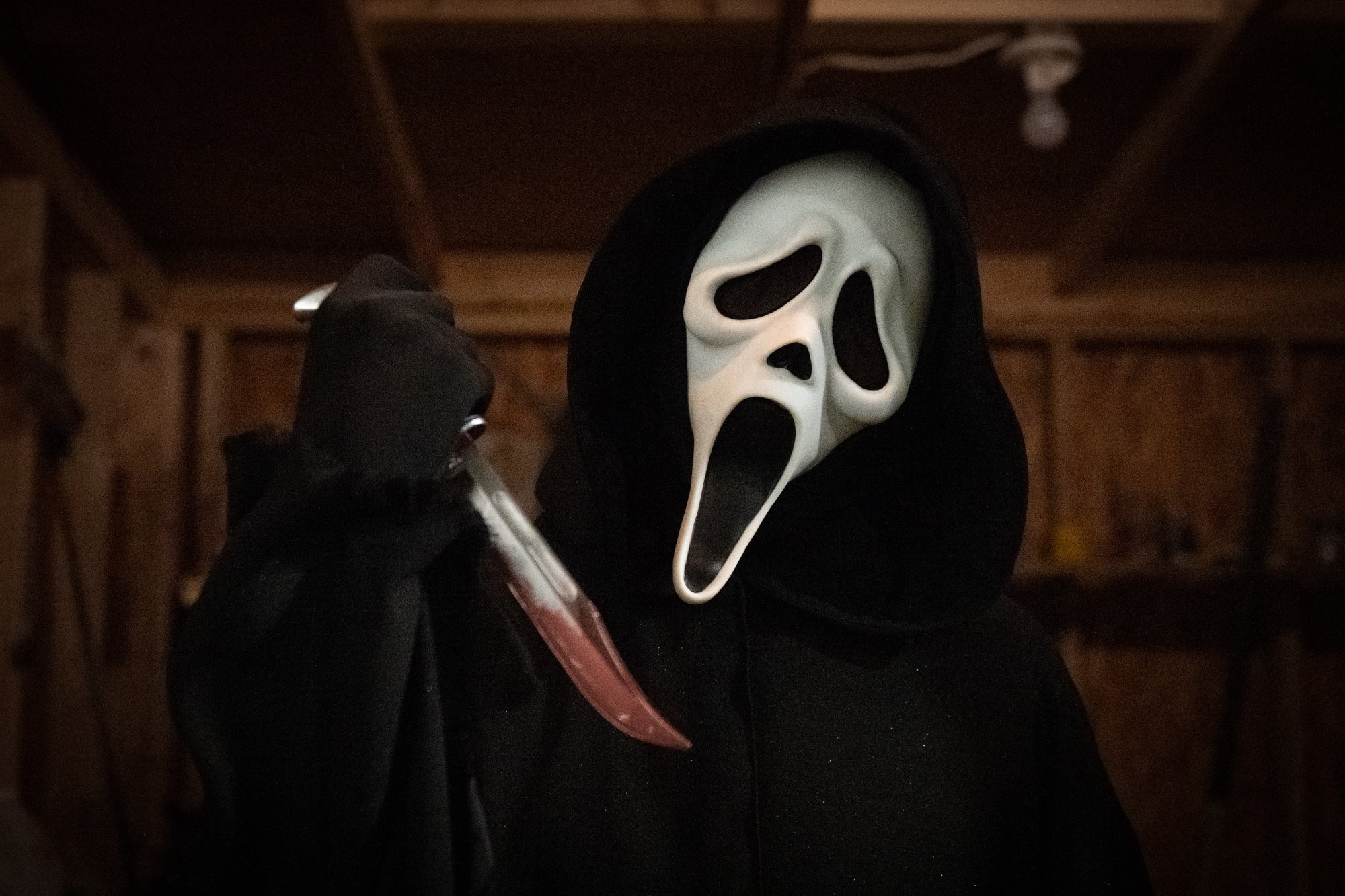 'Scream' Ghostface holding up a bloodied knife with their head tilted