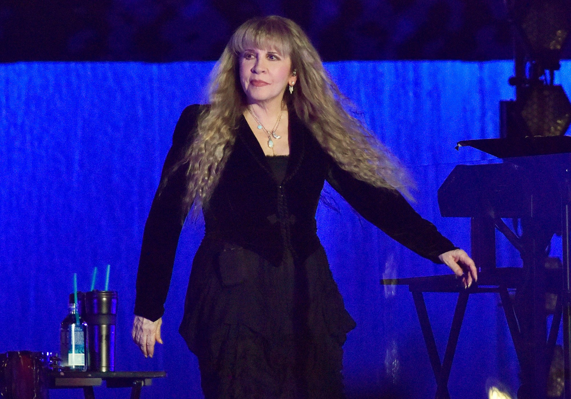 Stevie Nicks walks on stage wearing a long-sleeved black outfit