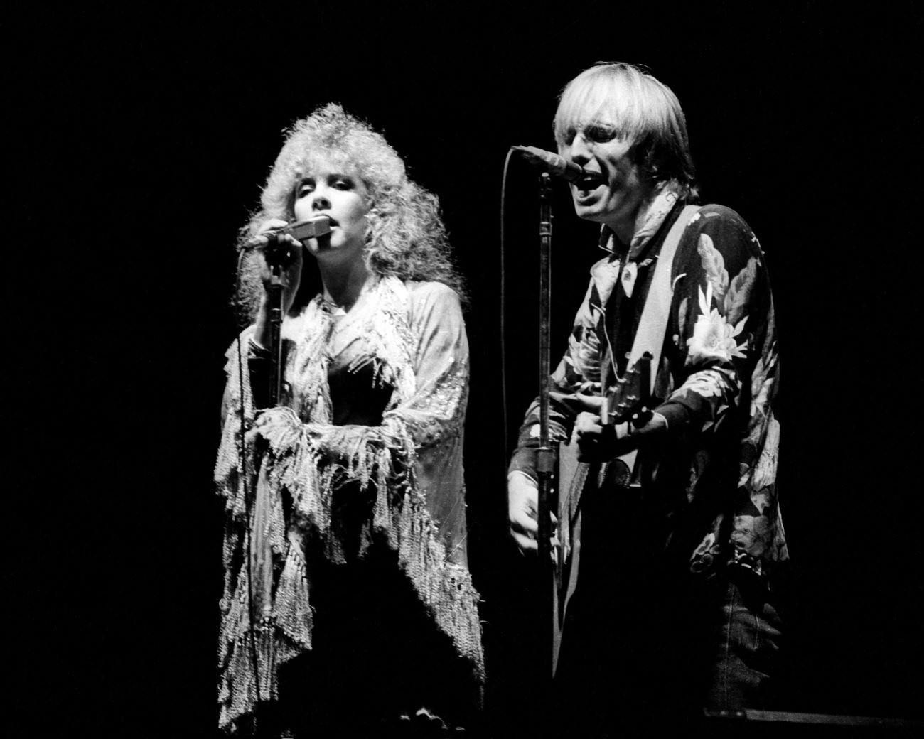 A black and white picture of Stevie Nicks and Tom Petty singing into microphones.