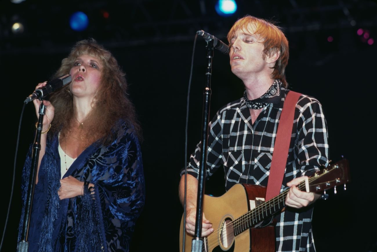 Stevie Nicks and Tom Petty sing into microphones. Petty plays guitar.