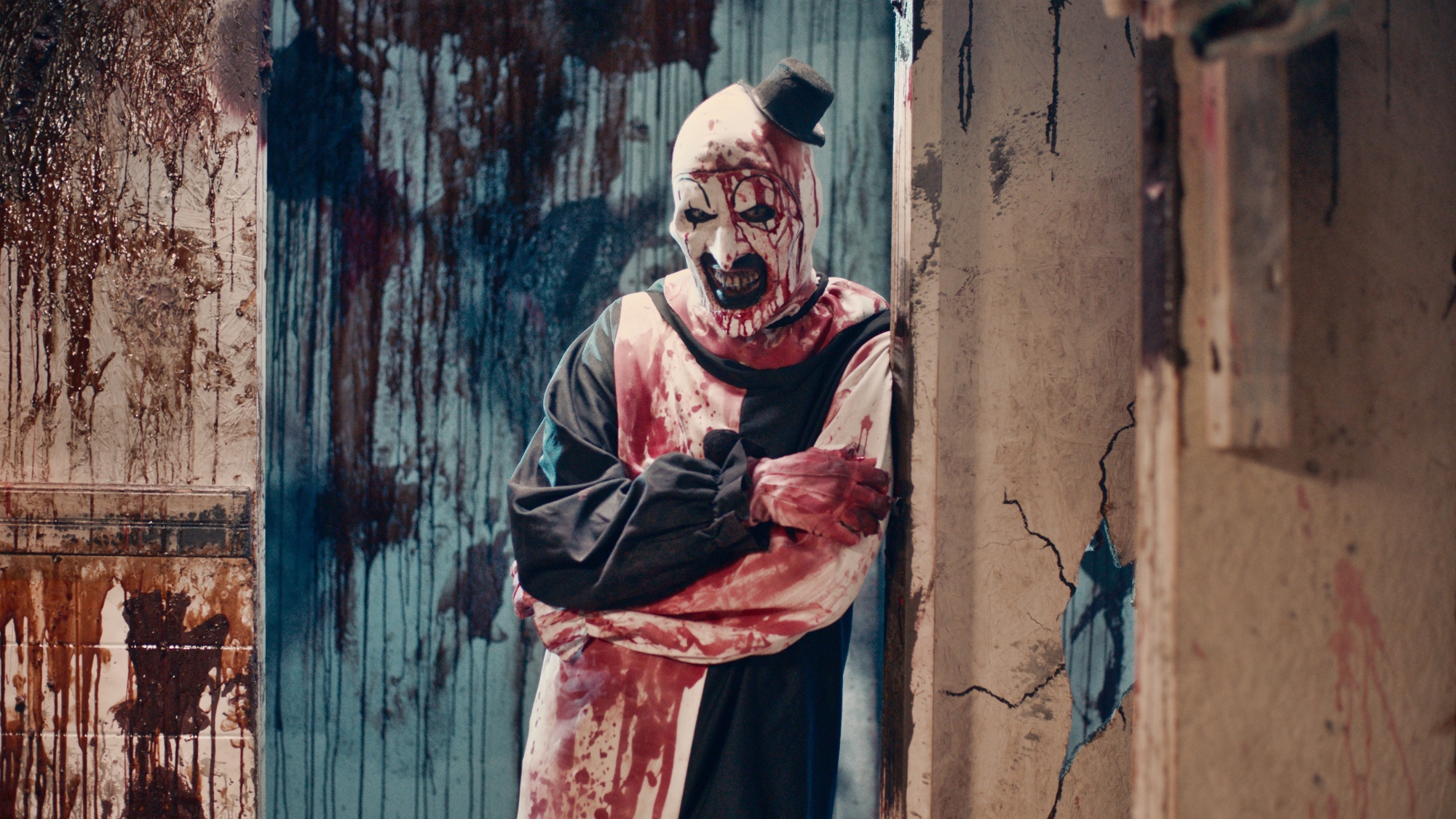 'Terrifier 2' David Howard Thornton as Art the Clown leaning against a door frame with his arms crossed covered in blood