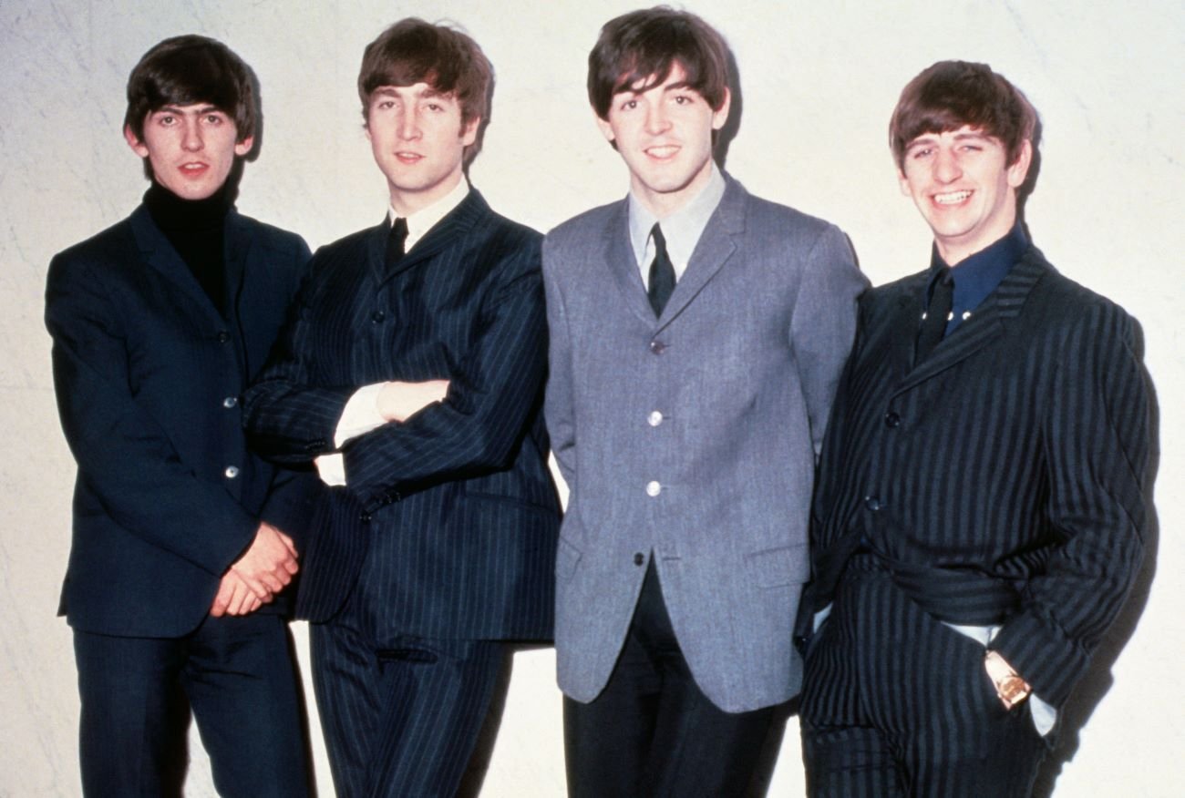 George Harrison, John Lennon, Paul McCartney, and Ringo Starr of The Beatles stand in a line, leaning against a wall.