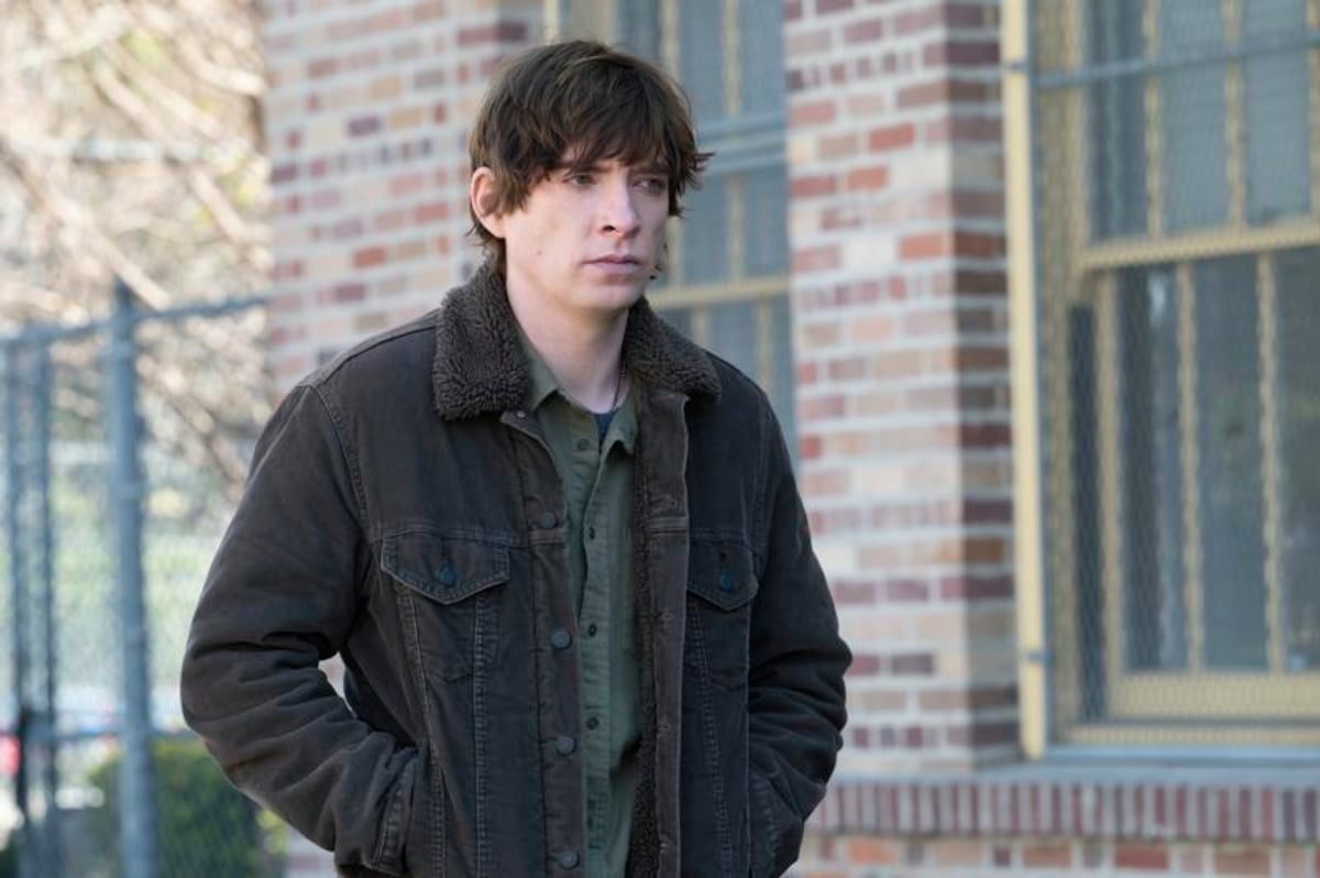 Sam takes an interest to the Kaddish in The Patient. Sam stands in front of a brick building with his hands in his jacket pockets. 