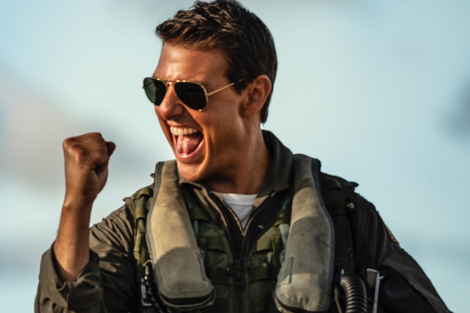 'Top Gun: Maverick' Tom Cruise as Maverick smiling with his mouth open, wearing aviator sunglasses and his uniform. He's holding his fist up in the air.