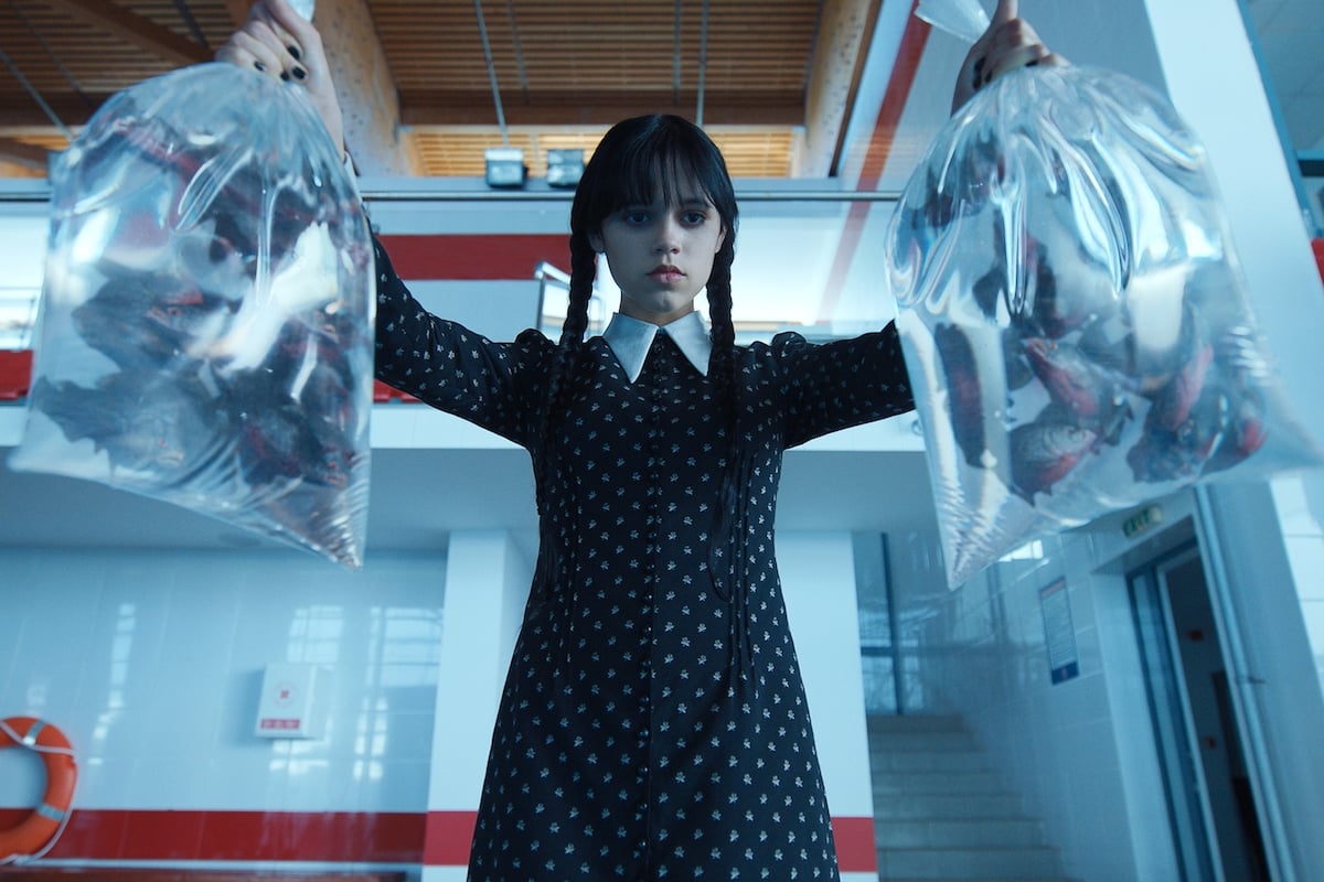 Wednesday Addams (Jenna Ortega) holds two plastic bags of piranhas