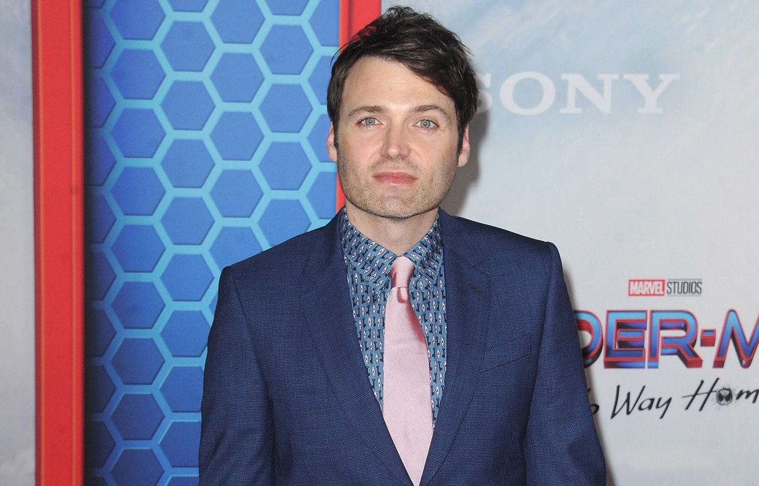 The Watcher Andrew Pierce actor Seth Gabel poses in front of a Spider-Man: No Way Home backdrop at the film premiere in 2021