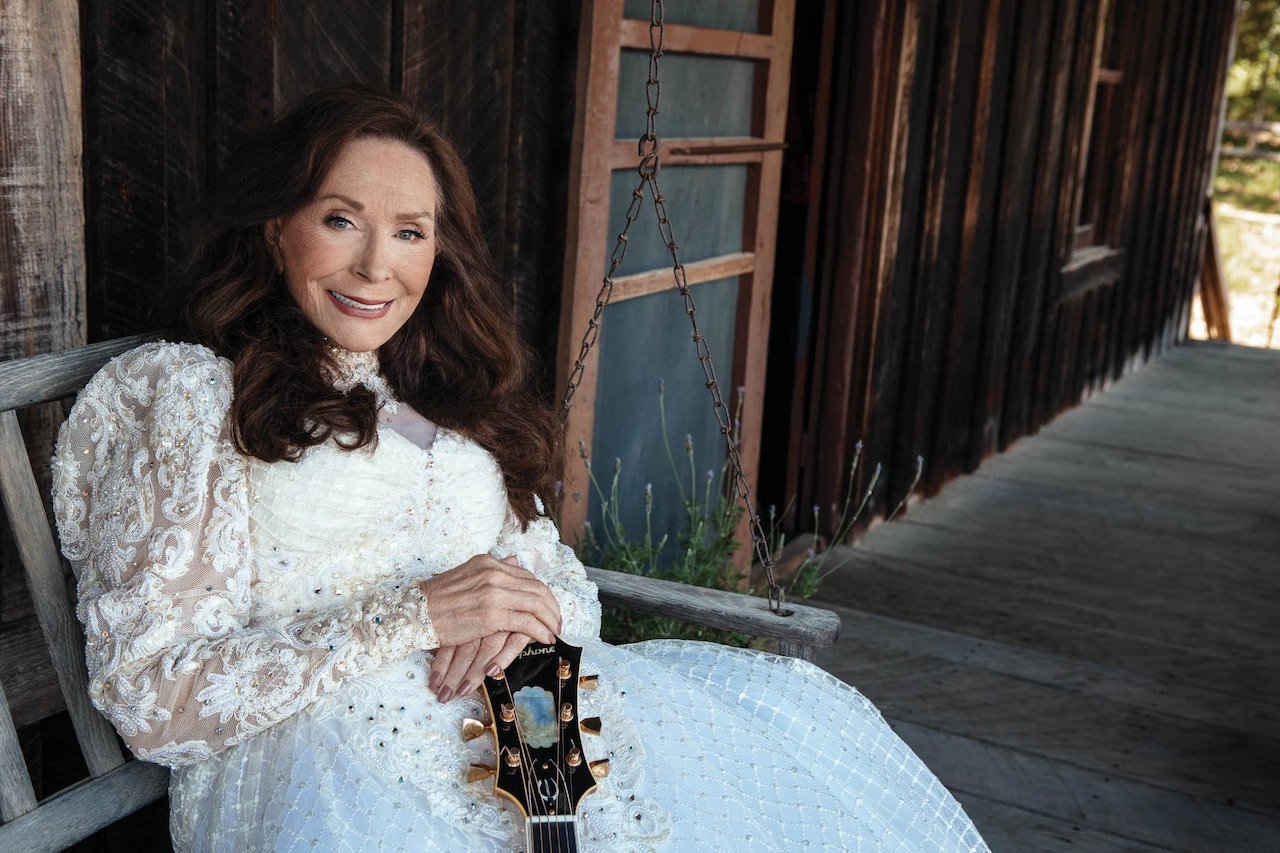 Loretta Lynn sitting on a porch, smiling. She once said her life went from misery to happiness, then back to misery.