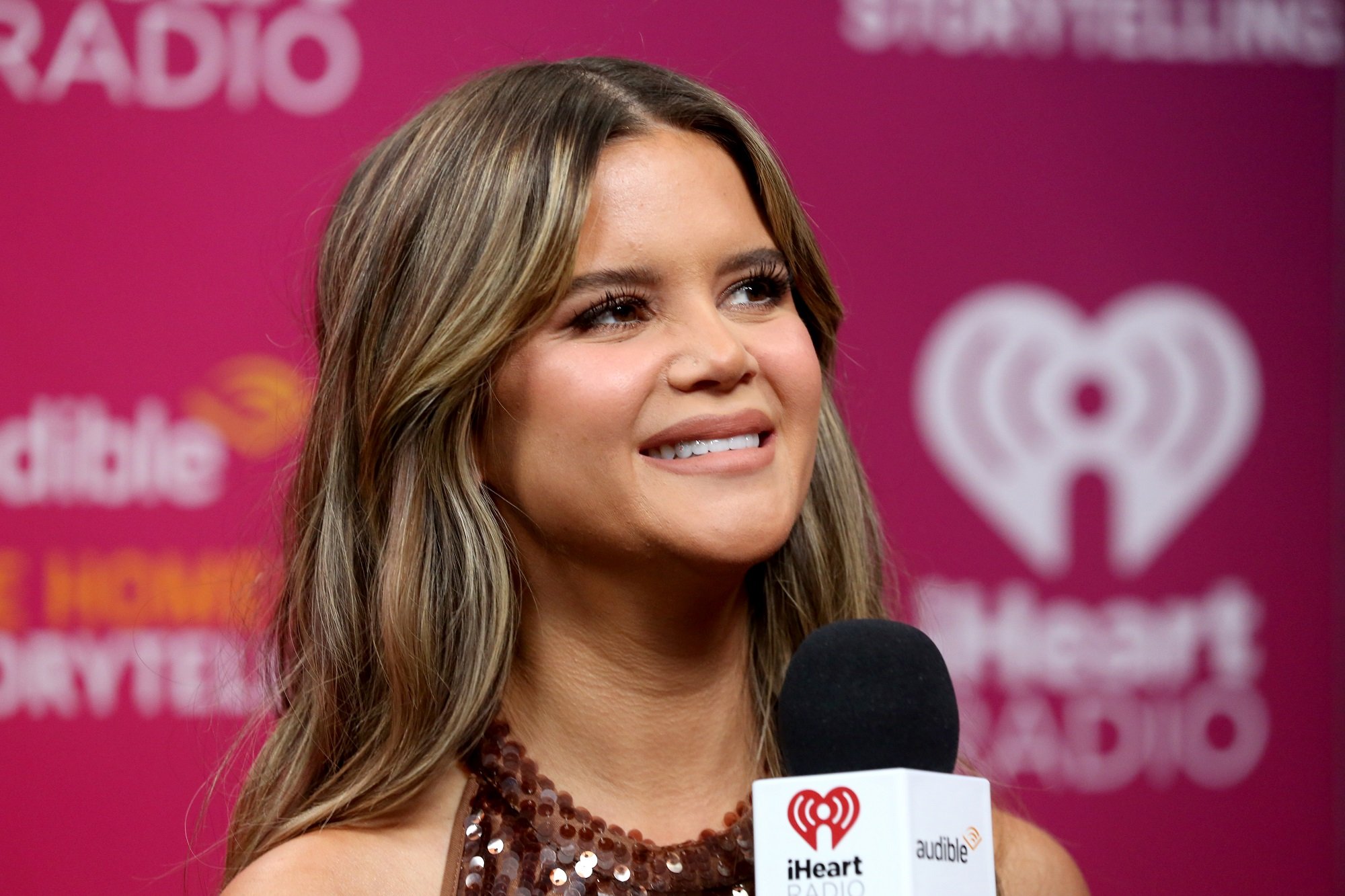 Maren Morris smiles in front of a pink 'iHeartRadio' backdrop