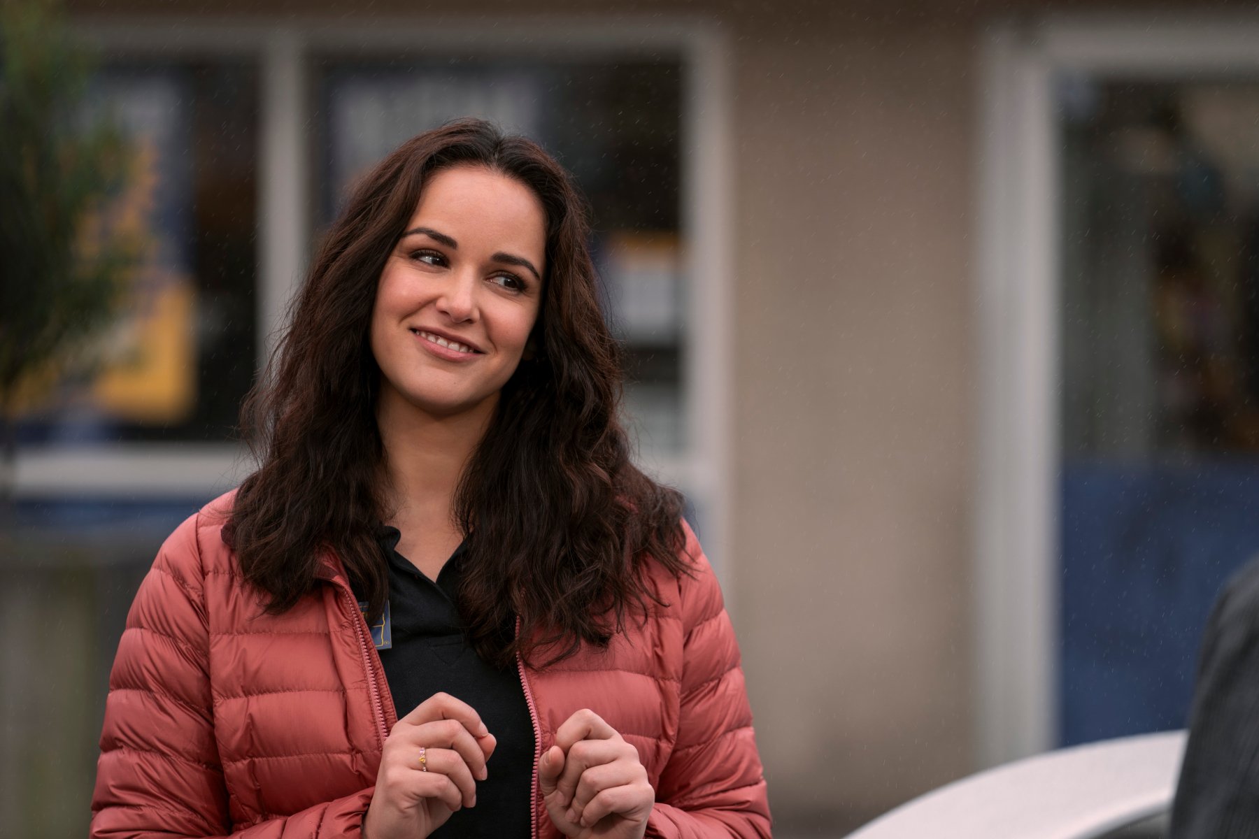 Melissa Fumero in 'Blockbuster' on Netflix for our article about the show and its take on connection. She's wearing a pink jacket and tilting her head.