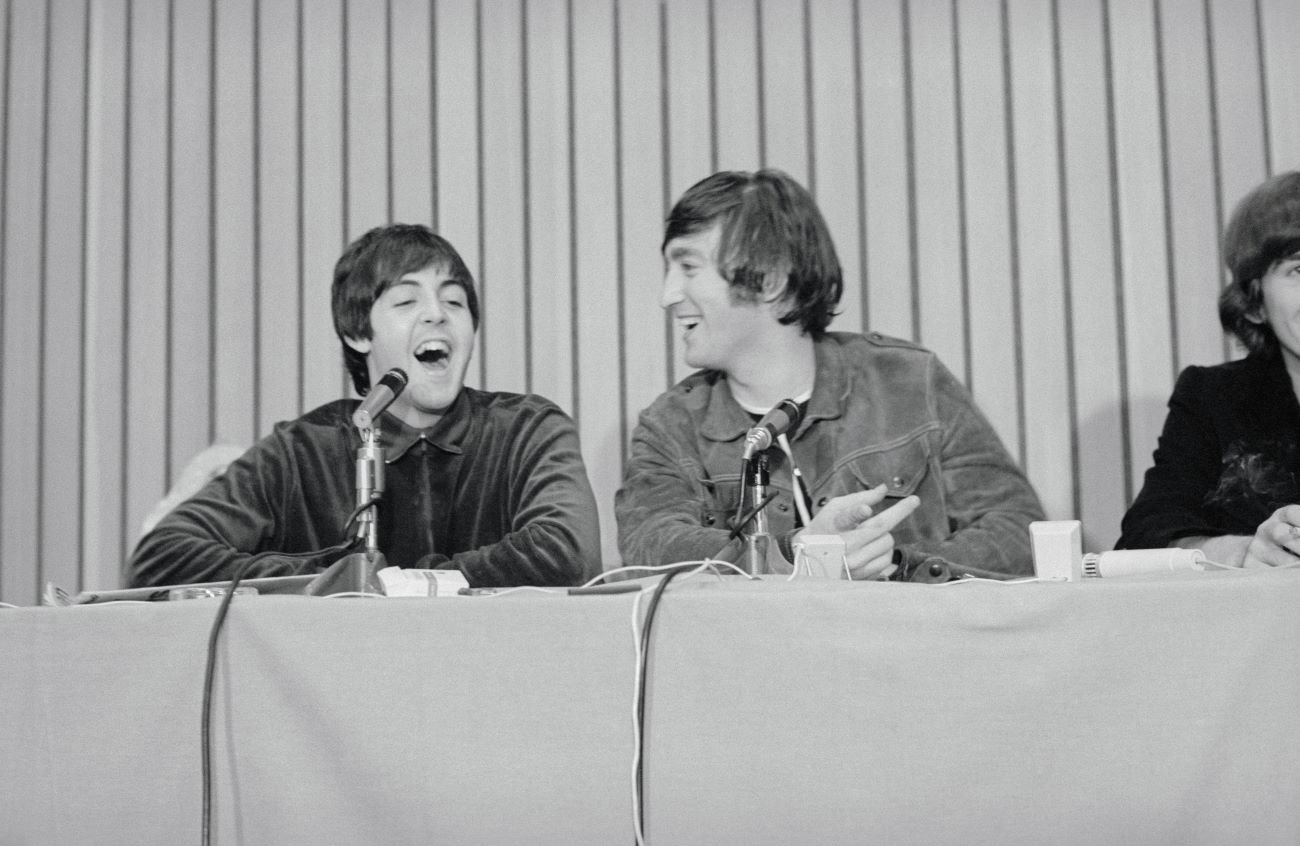 A black and white picture of Paul McCartney and John Lennon sitting at a table in front of microphones.