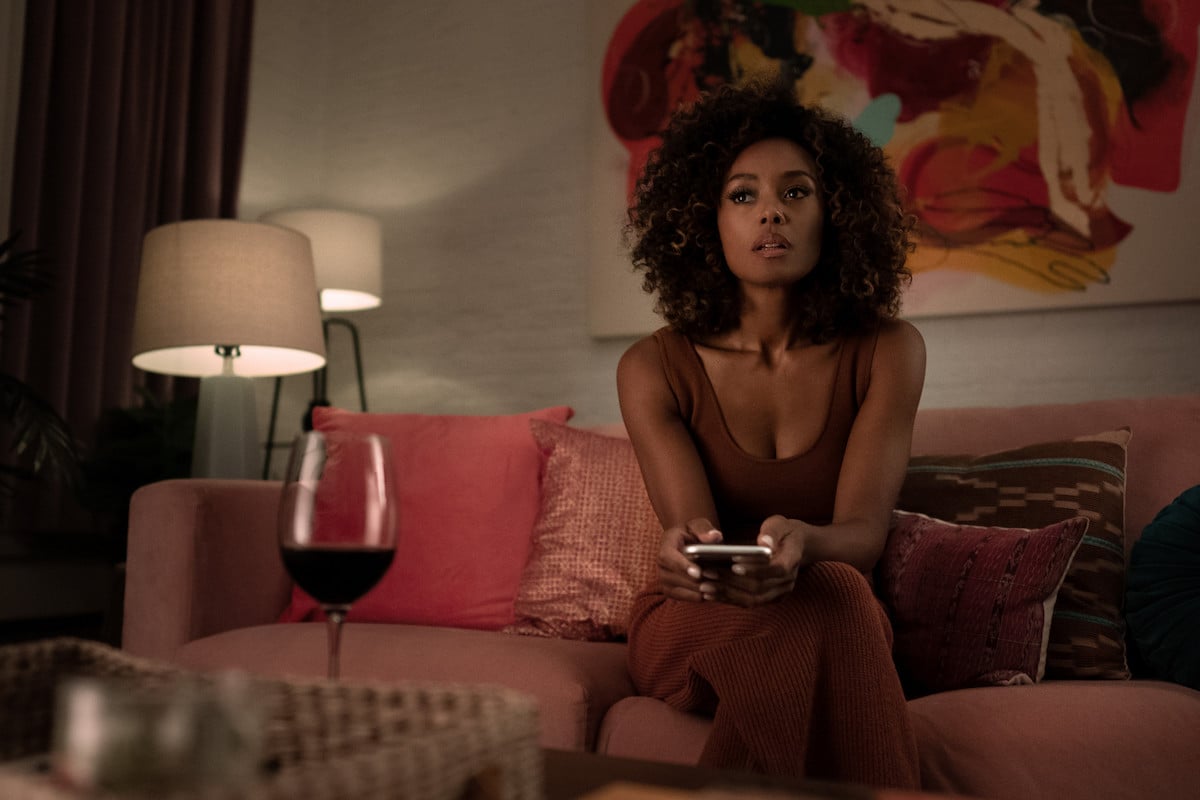 Melanie Liburd as Carrie Milgram watching TV in a red lounge outfit in 'Power Book II: Ghost'