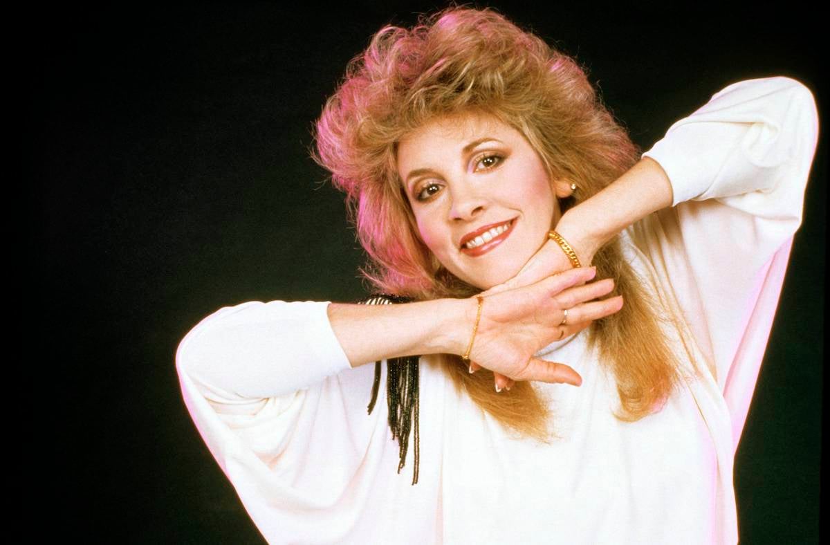 Stevie Nicks, who said she wouldn't want to return to the 1980s, smiles and poses in a white outfit.