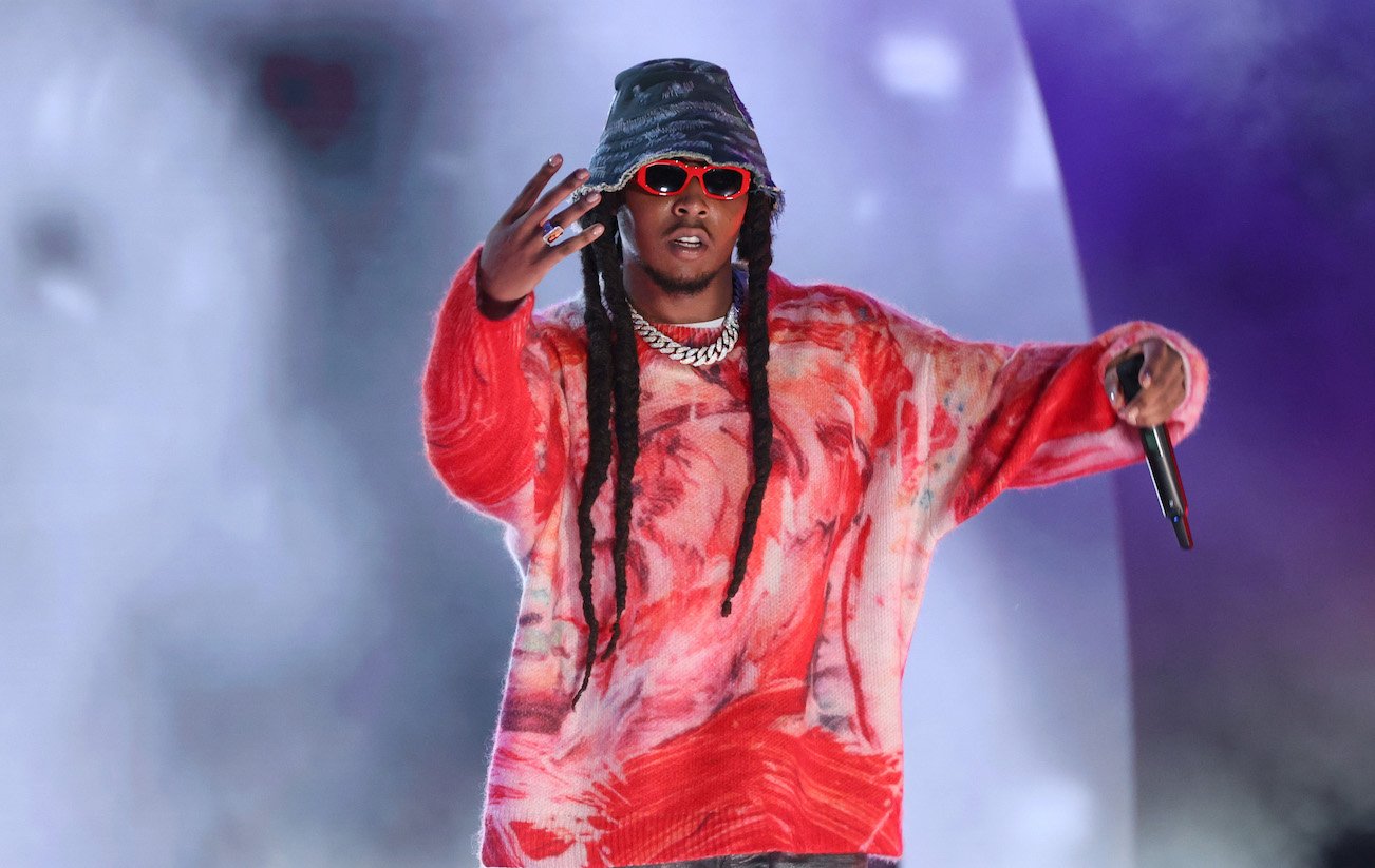 Migos rapper Takeoff wearing a red sweatshirt and a bucket hat on stage