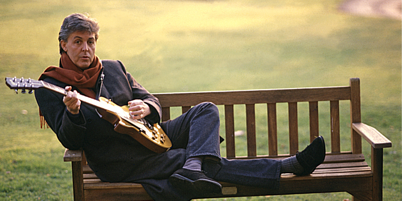 Former Beatles bassist Paul McCartney sits on a bench playing guitar.