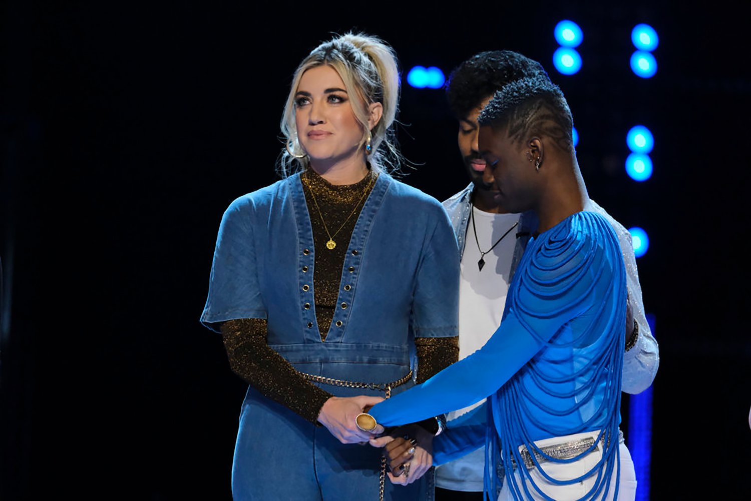 Morgan Myles, Devix, and Eric Who huddle together and hold hands as they wait to see who made it to the Top 10 on The Voice Season 22.