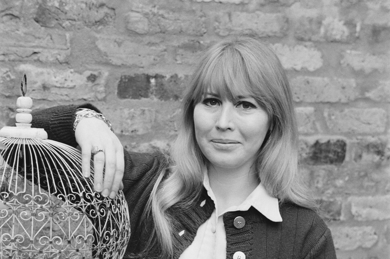 A black and white picture of Cynthia Lennon standing with her arm resting on a cage.