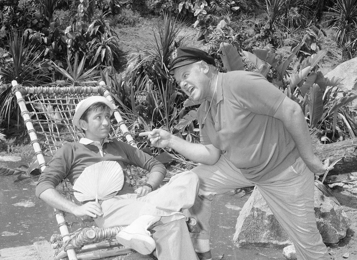 'Gilligan's Island' star Bob Denver sitting in a bamboo chair and Alan Hale Jr. standing in a scene from the sitcom.