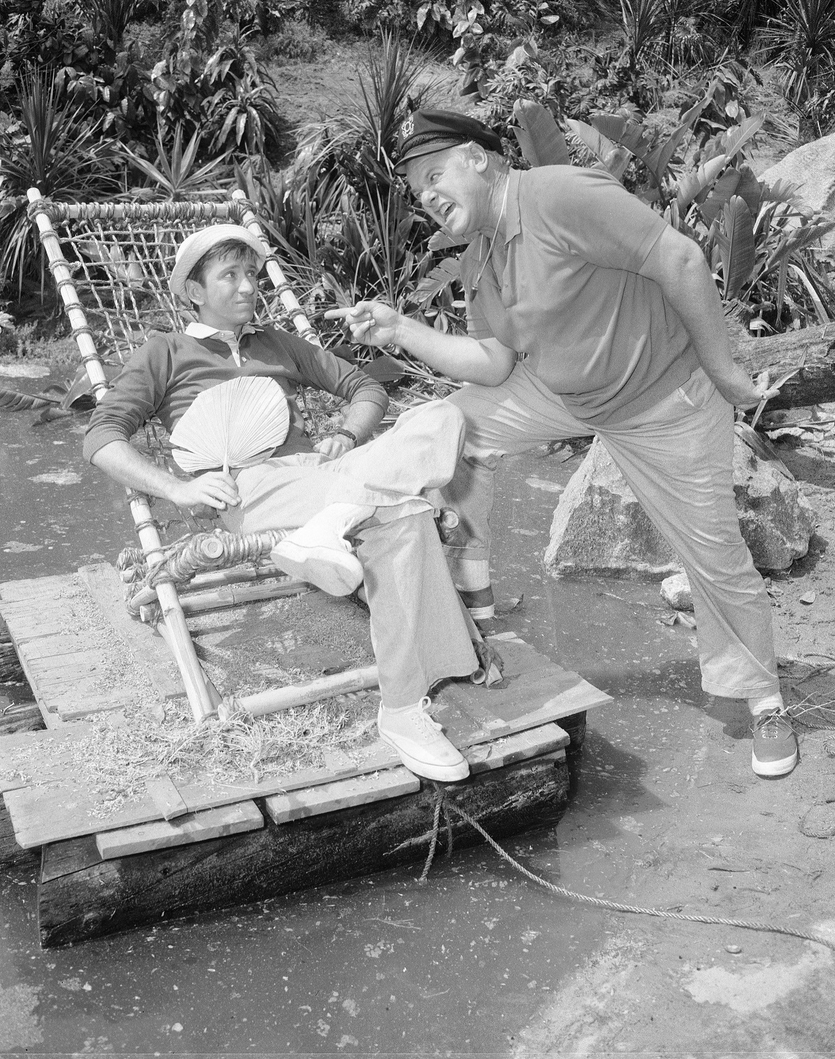 'Gilligan's Island' star Bob Denver sitting in a bamboo chair and Alan Hale Jr. standing in a scene from the sitcom.