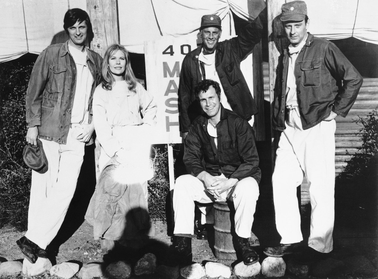 A black and white photo of Alan Alda Loretta Swit, Mike Farrell (sitting), McLean Stevenson, and Larry Linville from 'M*A*S*H'