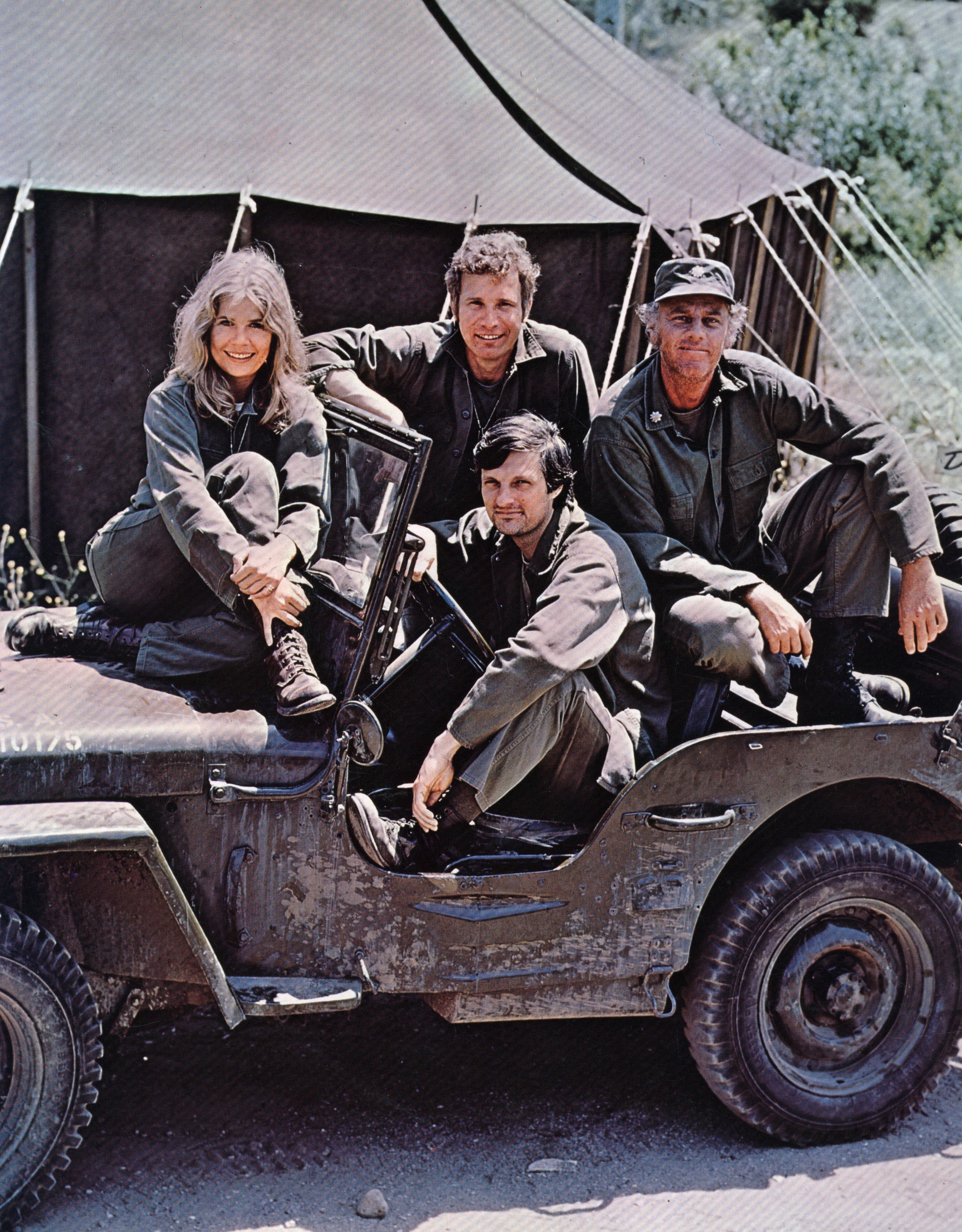 The cast of 'M*A*S*H' dressed in their Army uniforms and sitting in a Jeep during a promotional photo from the series.