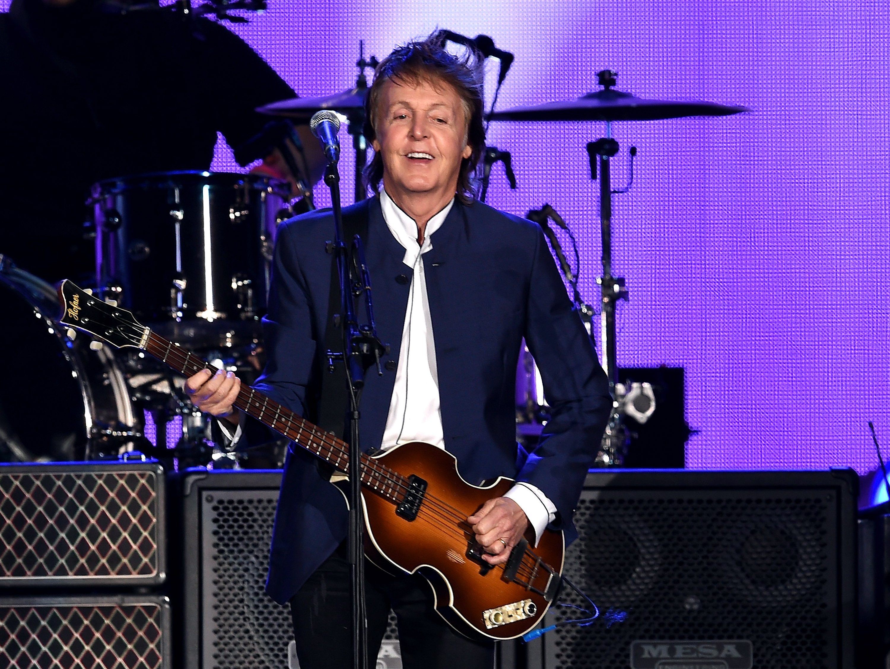 Paul McCartney stands onstage and holds a guitar.