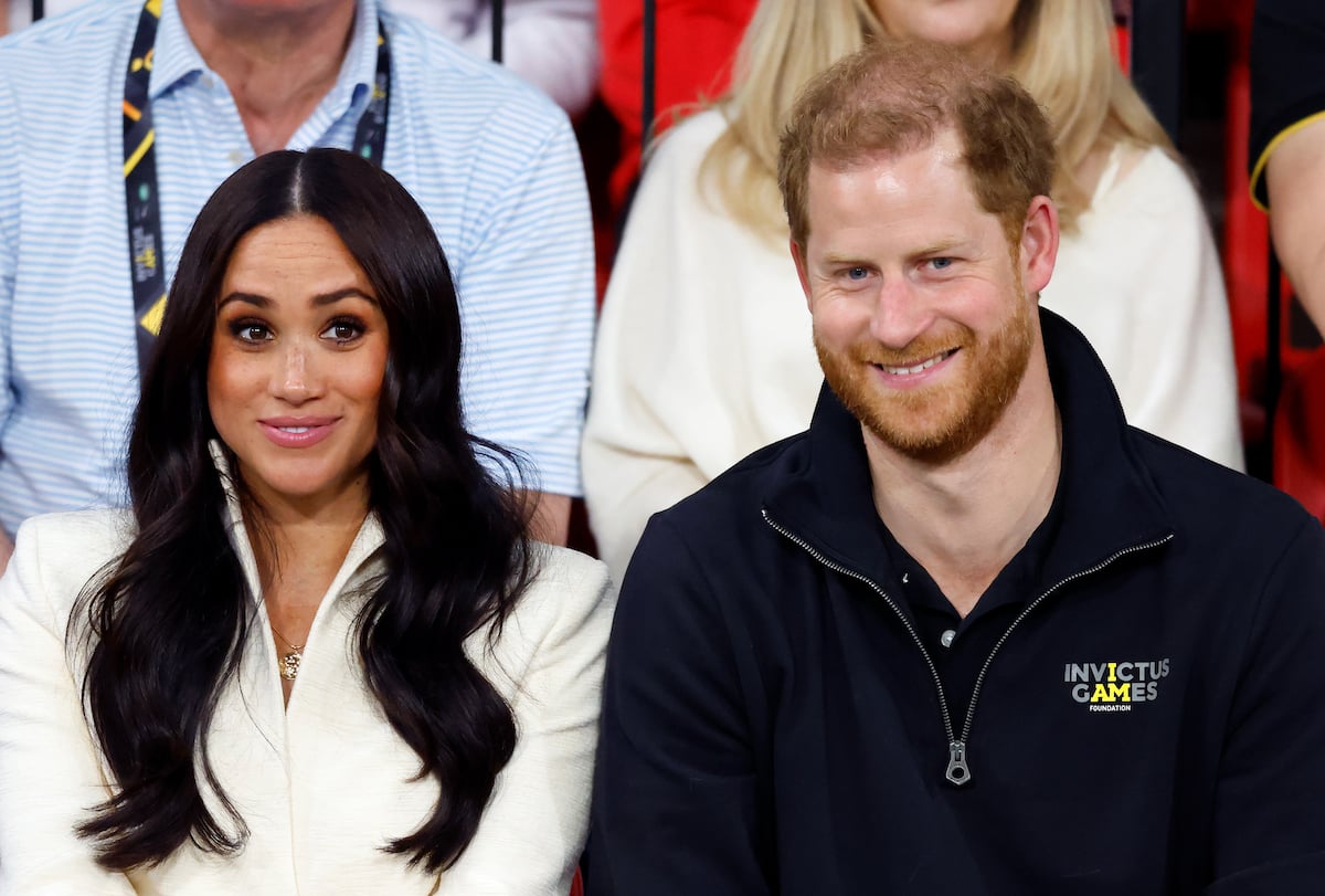 Meghan Markle and Prince Harry, who discussed his ex-girlfriends in their new Netflix documentary, smile together while seated at an event.