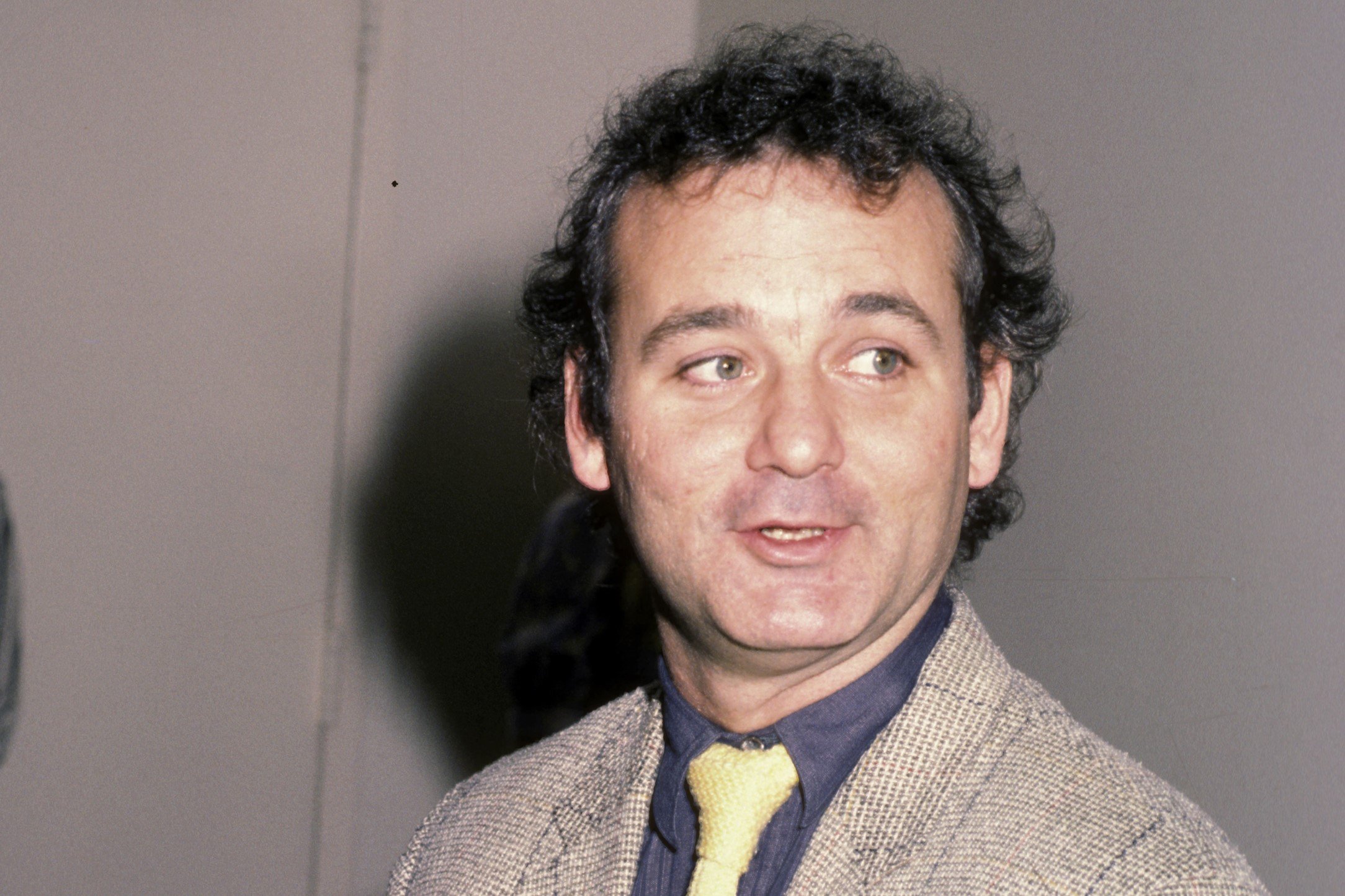 Bill Murray, who was a part of the 'Scrooged' cast, wears a light gray tweed suit over a dark blue button-up shirt and light yellow tie.