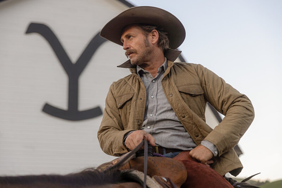 Josh Lucas as Young John Dutton in Yellowstone Season 5. John wears a cowboy hat and tan jacket and sits on top of a horse. 