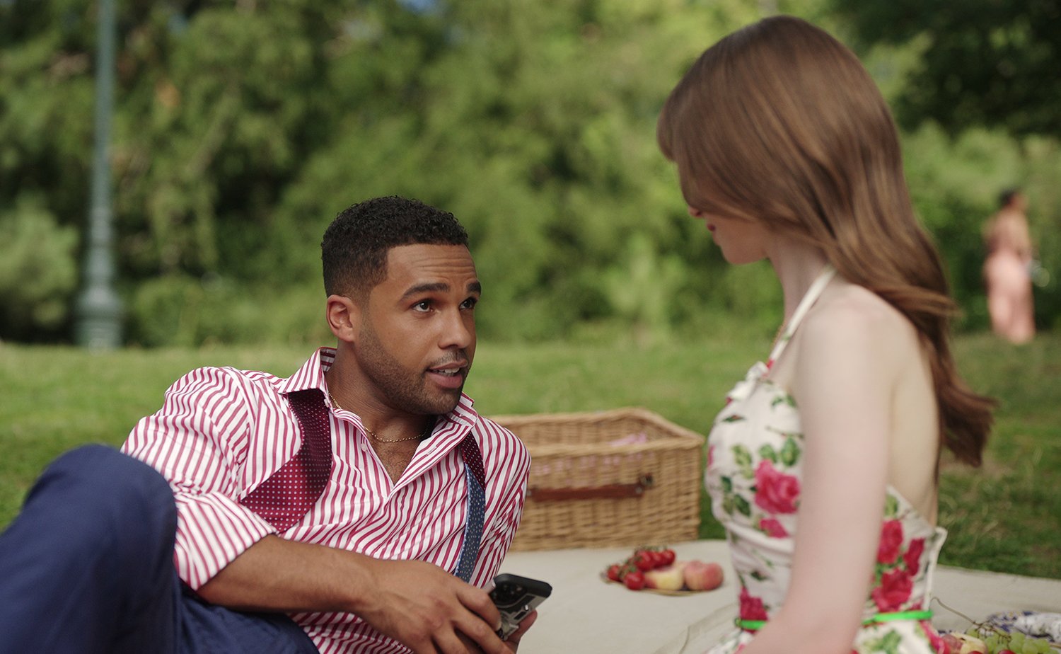 Emily in Paris Season 3: Lucien Laviscount as Alfie and Lily Collins as Emily sitting together on a picnic blanket in a park