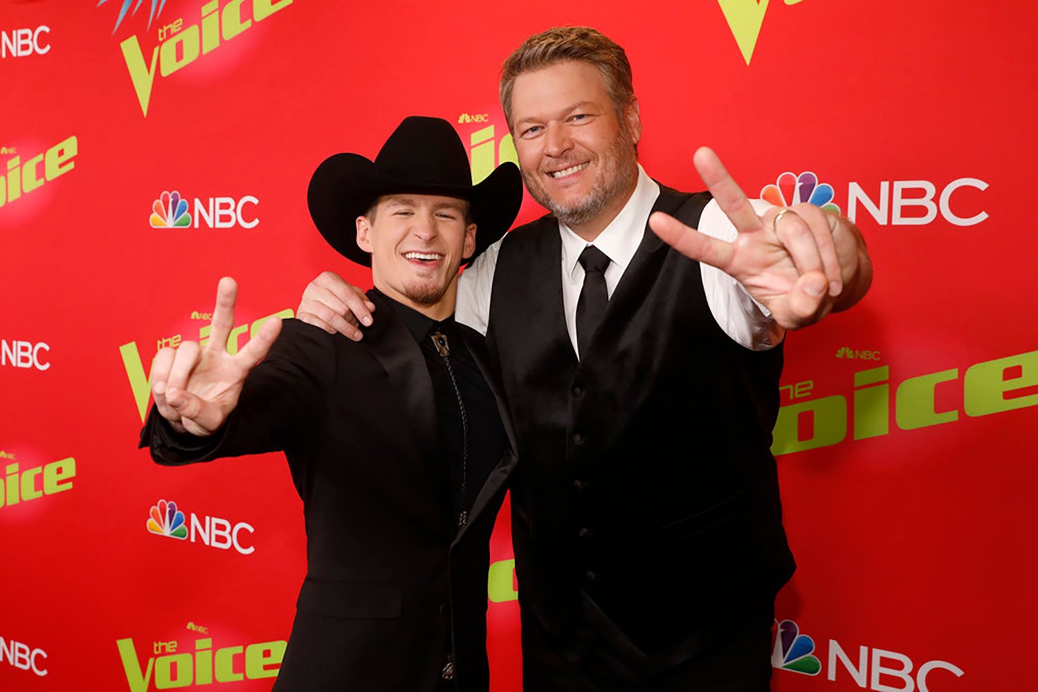 The Voice 2022 winner Bryce Leatherwood and his coach, Blake Shelton, hold up 'V' signs with their fingers in front of a red backdrop