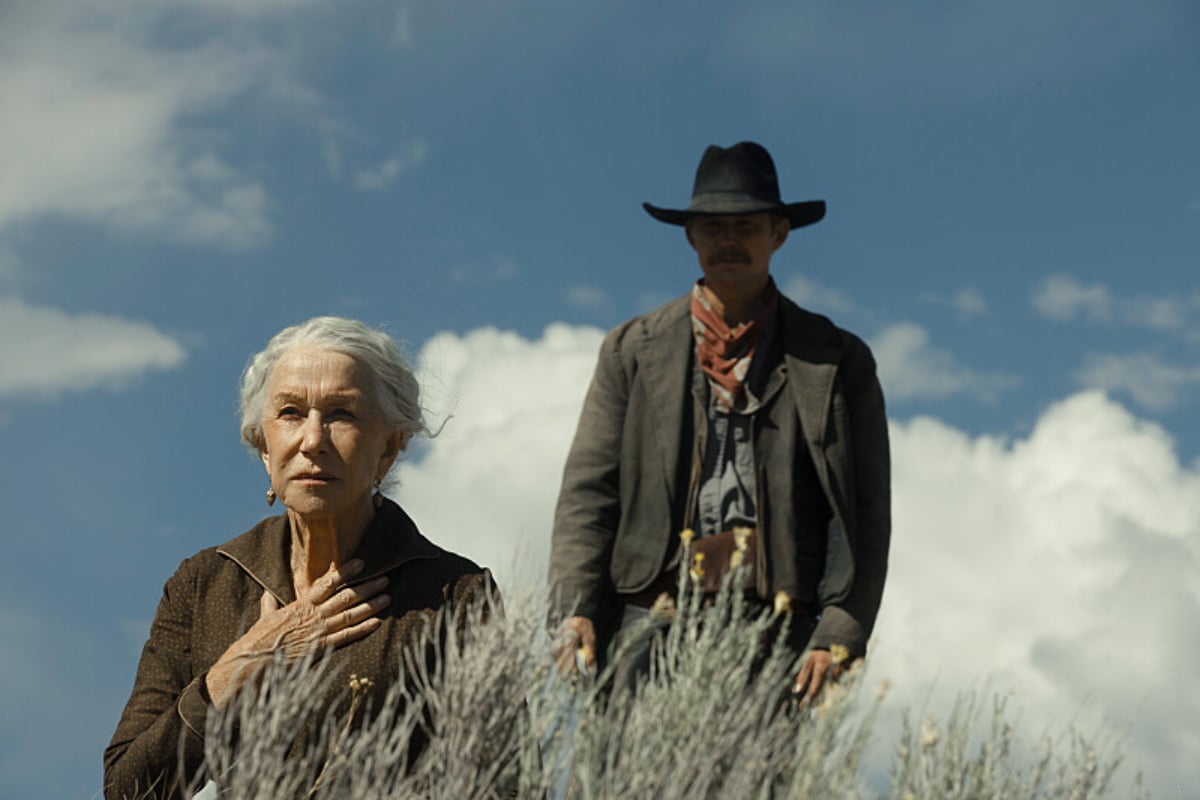 1923 Episode 5 premieres in February. Cara Dutton kneels in the grass while Zane stands behind her. 