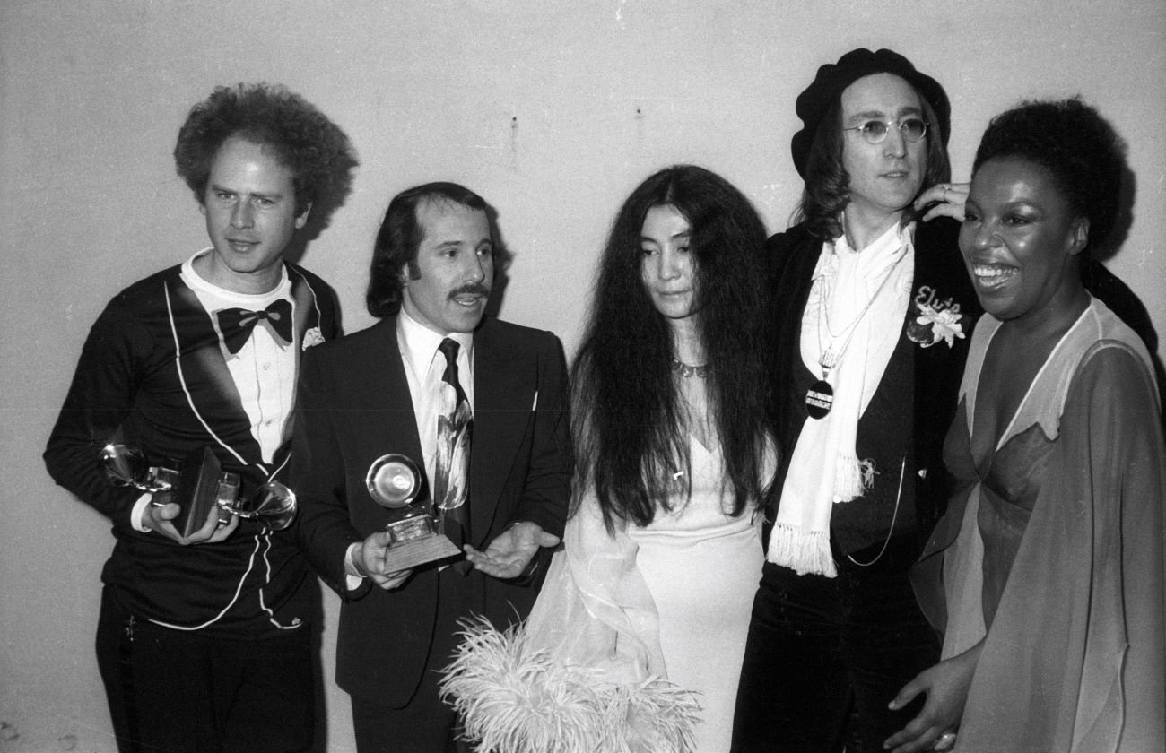 A black and white picture of Art Garfunkel, Paul Simon, Yoko Ono, John Lennon, and Roberta Flack. Simon and Garfunkel hold Grammy awards.