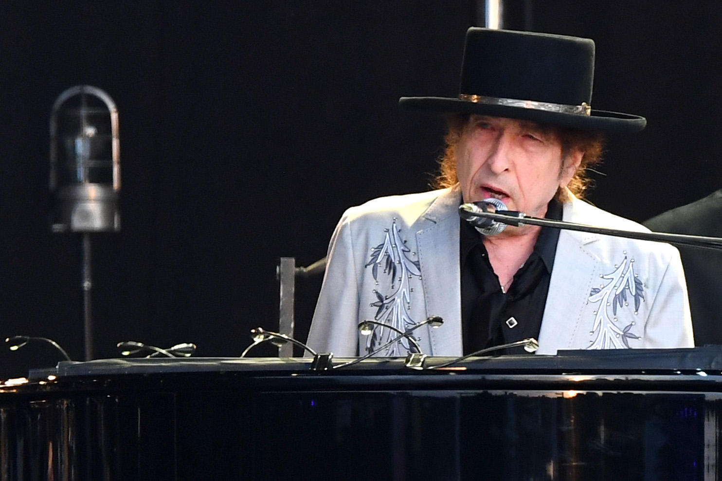 Bob Dylan wears a hat and sits at a piano.