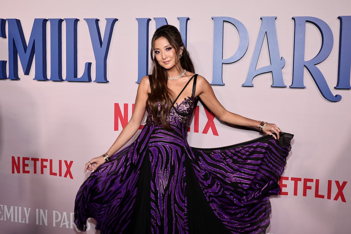 Ashley Park twirls her dress in front of an "Emily in Paris" backdrop.