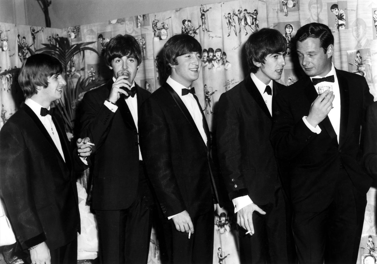 A black and white picture of The Beatles standing in a line behind Brian Epstein. 