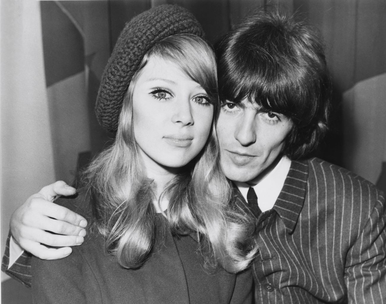 A black and white picture of George Harrison with his arm around his wife Pattie Boyd's shoulders.